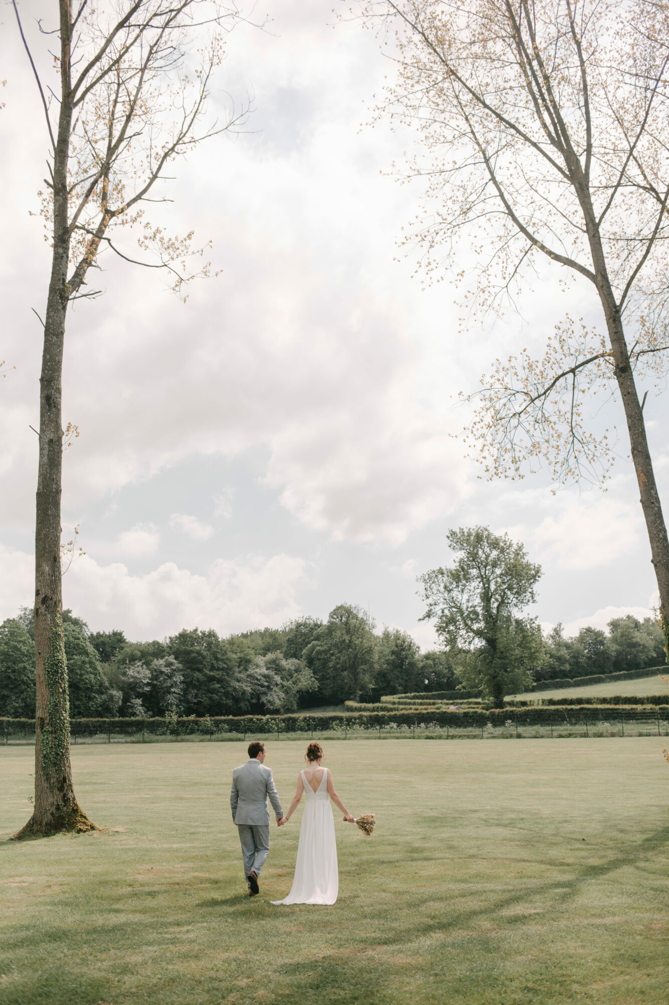 Thibaud et Aline – Couple-74 Mariés se promenant main dans la main dans le parc du Domaine de la Traxène. Un cadre naturel et paisible au cœur de 11 hectares de verdure, idéal pour des photos de mariage authentiques et intemporelles.