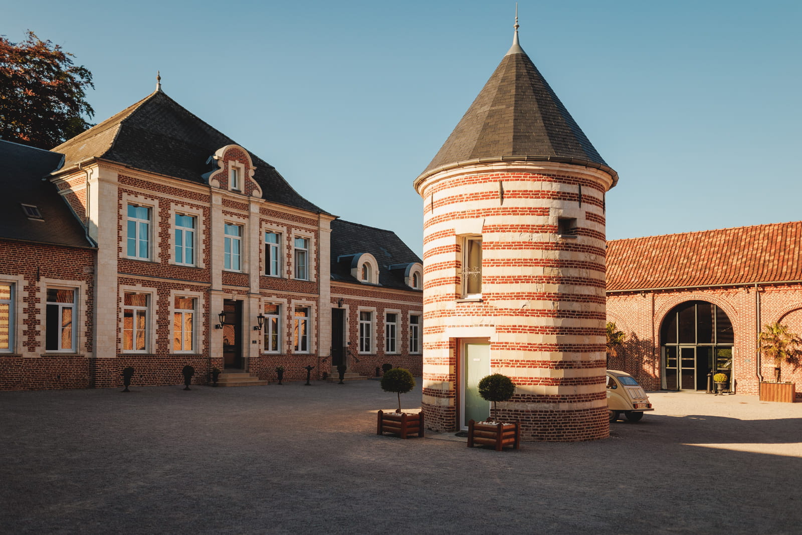 renaud julian copie Vue extérieure du Domaine de la Traxène, lieu de réception de mariage dans le Pas-de-Calais, avec sa cour pavée, sa tour en briques typique et ses élégants bâtiments de caractère au cœur d’un domaine d’exception.