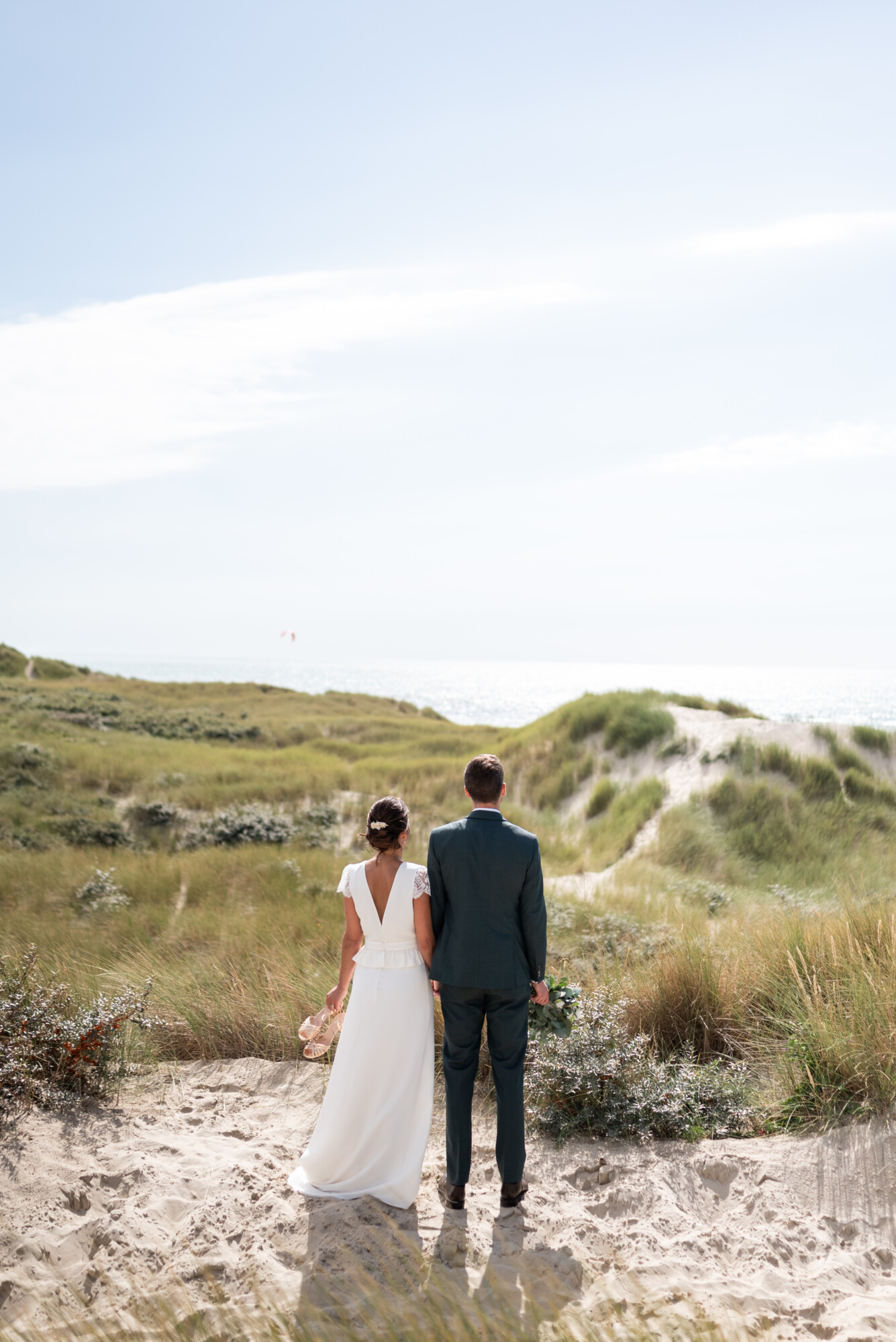 Séance photo de mariage sur la Côte d’Opale, à proximité du Domaine de la Traxène, avec les mariés contemplant les dunes et la mer pour immortaliser leur union dans un cadre naturel d’exception.