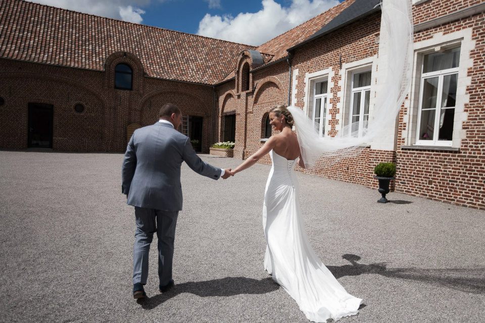 DOMAINE (26) (1) Mariés se tenant la main dans la cour du Domaine de la Traxène, un cadre authentique et élégant pour célébrer un mariage près de la Côte d’Opale.