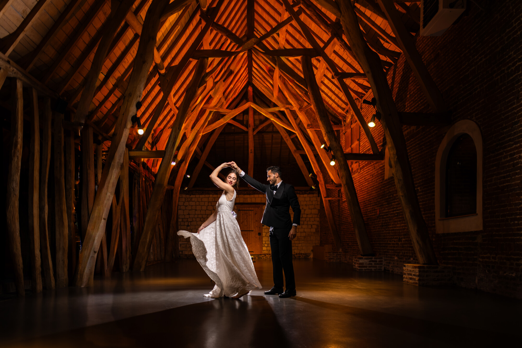 Mariés dansant sous une majestueuse charpente en bois lors de leur réception de mariage.