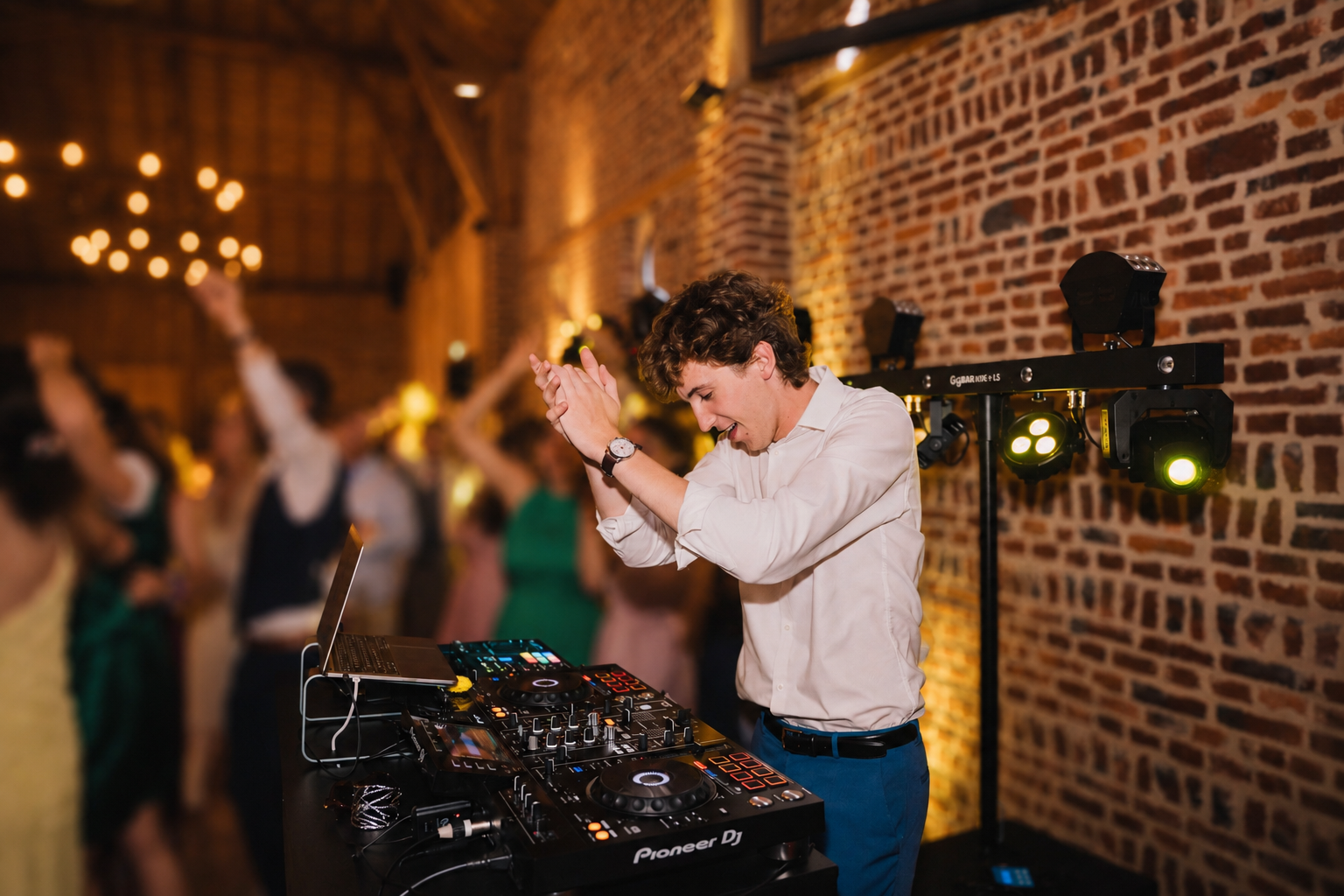 DJ animant une soirée de mariage derrière ses platines, avec les invités dansant en arrière-plan dans la salle de réception du Domaine de la Traxène.