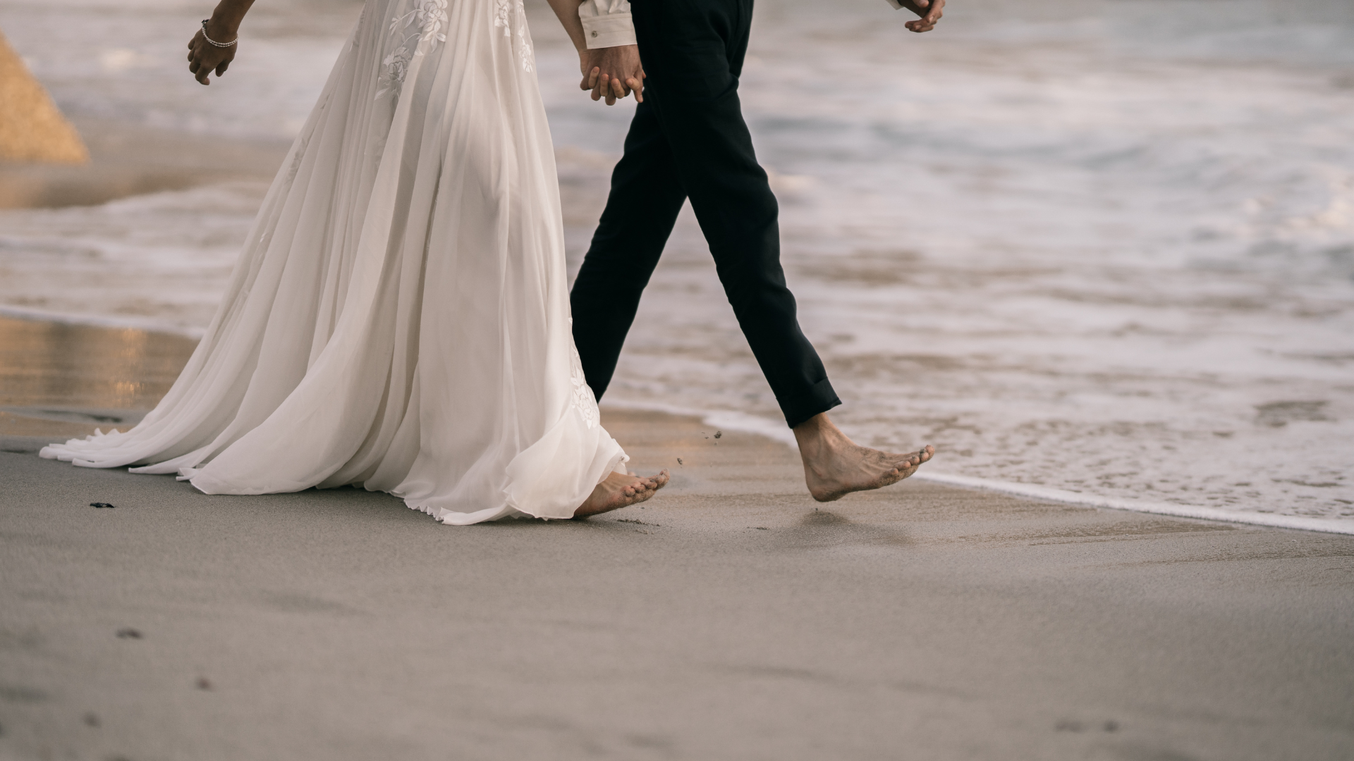 Mariage au Touquet-Paris-Plage, avec un couple de jeunes mariés marchant pieds nus main dans la main sur la plage, au bord de la mer.